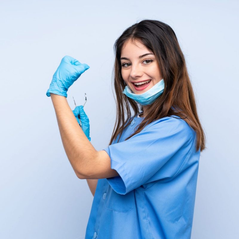 Woman dentist holding tools over isolated blue background making strong gesture